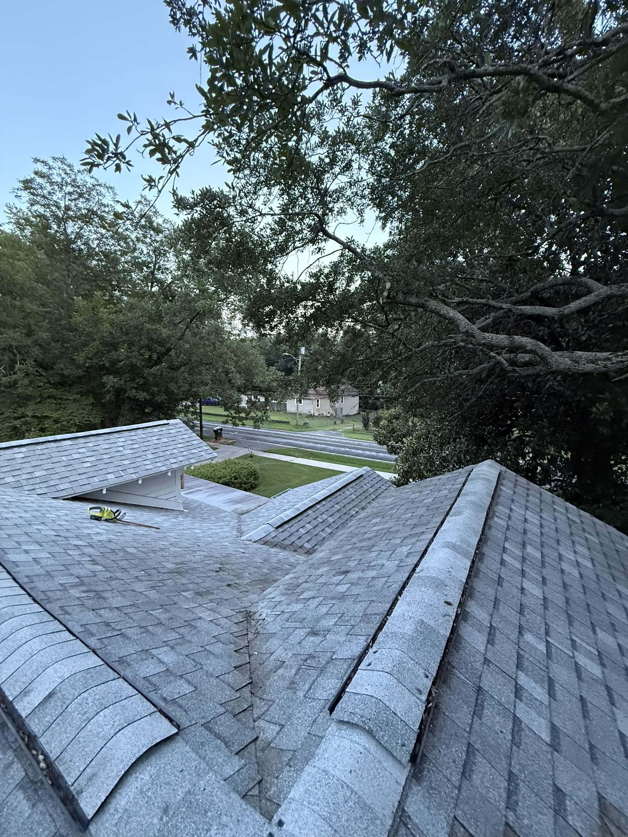 The same roof at dusk with every valley swept clear, a hedge trimmer resting on the shingles